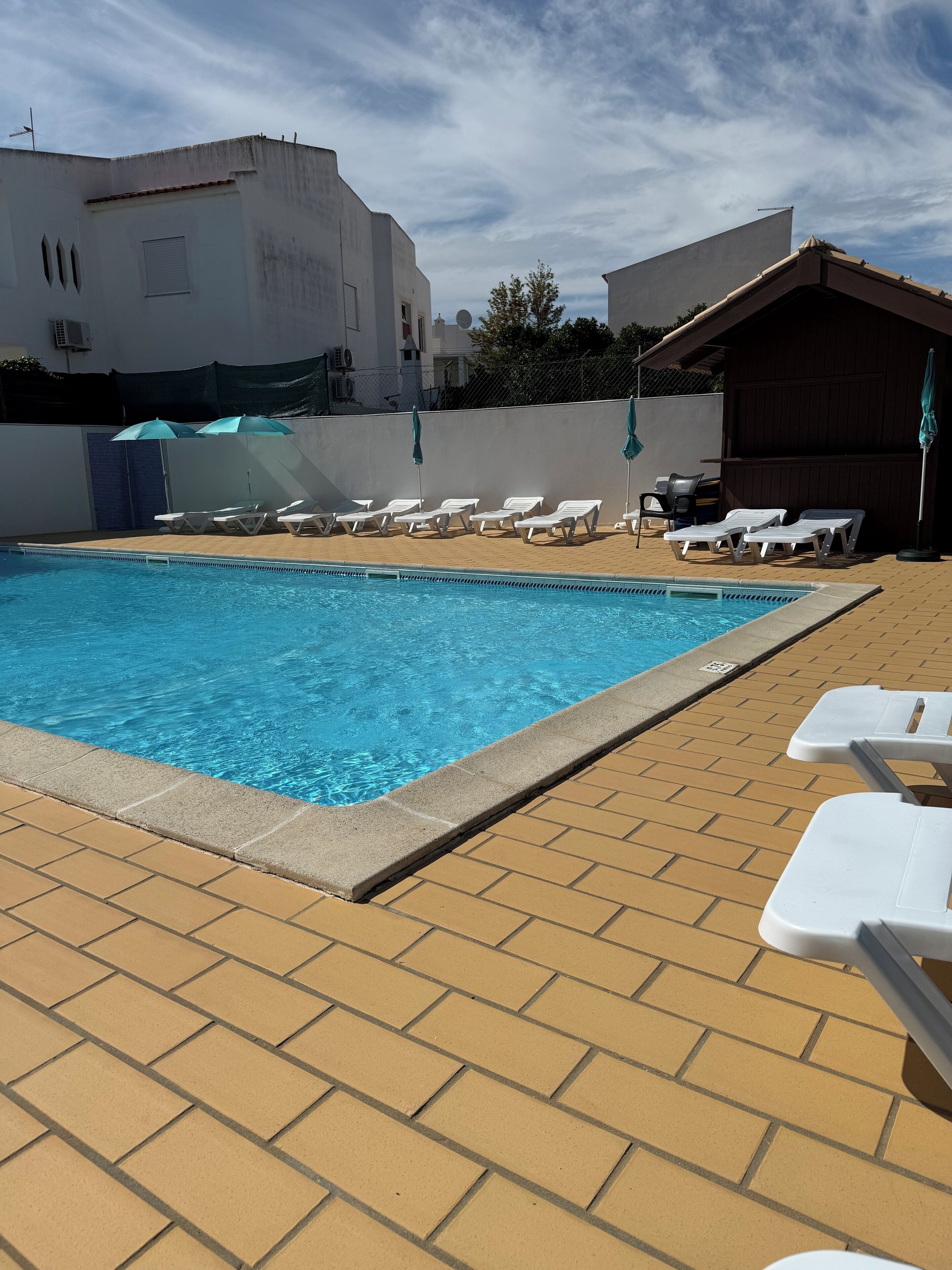 A swimming pool with lounge chairs and umbrellas, surrounded by buildings.