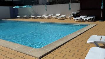 A swimming pool with lounge chairs and umbrellas, surrounded by buildings.