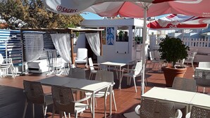 Un área de patio al aire libre con mesas y sillas blancas, sombrillas y una planta en maceta.