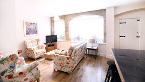 A living room with floral upholstery, a flat-screen TV, and a stone accent wall. - Stable Cottage (Harrogate)