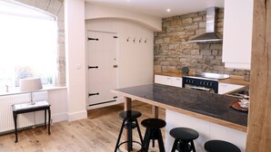 A modern kitchen with a stone wall, white cabinetry, and a central island with stools. - Stable Cottage (Harrogate)