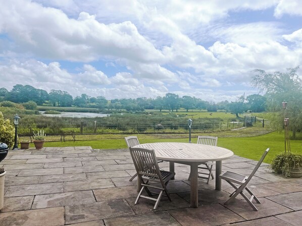A patio with a round table and chairs, a view of a lake, and a grassy landscape. - 2 bedroom accommodation in Whitechapel, near Preston (Whitechapel, near Preston)