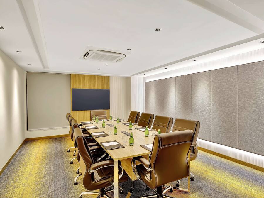 A conference room with a long table, brown leather chairs, and a large window with blinds.