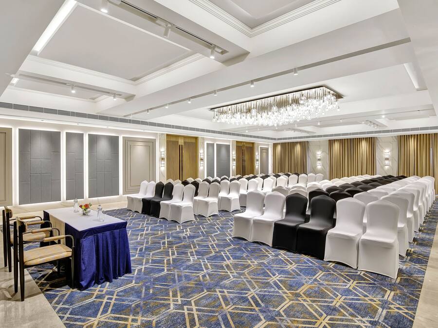 A conference room with rows of chairs, a table with a blue tablecloth, and a patterned carpet.