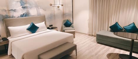 A modern hotel room with a large bed, a bench, a small table, and a sofa.