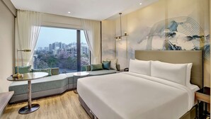 Una habitación de hotel moderna con una cama grande, una zona de estar con vistas y un paisaje urbano a través de la ventana.