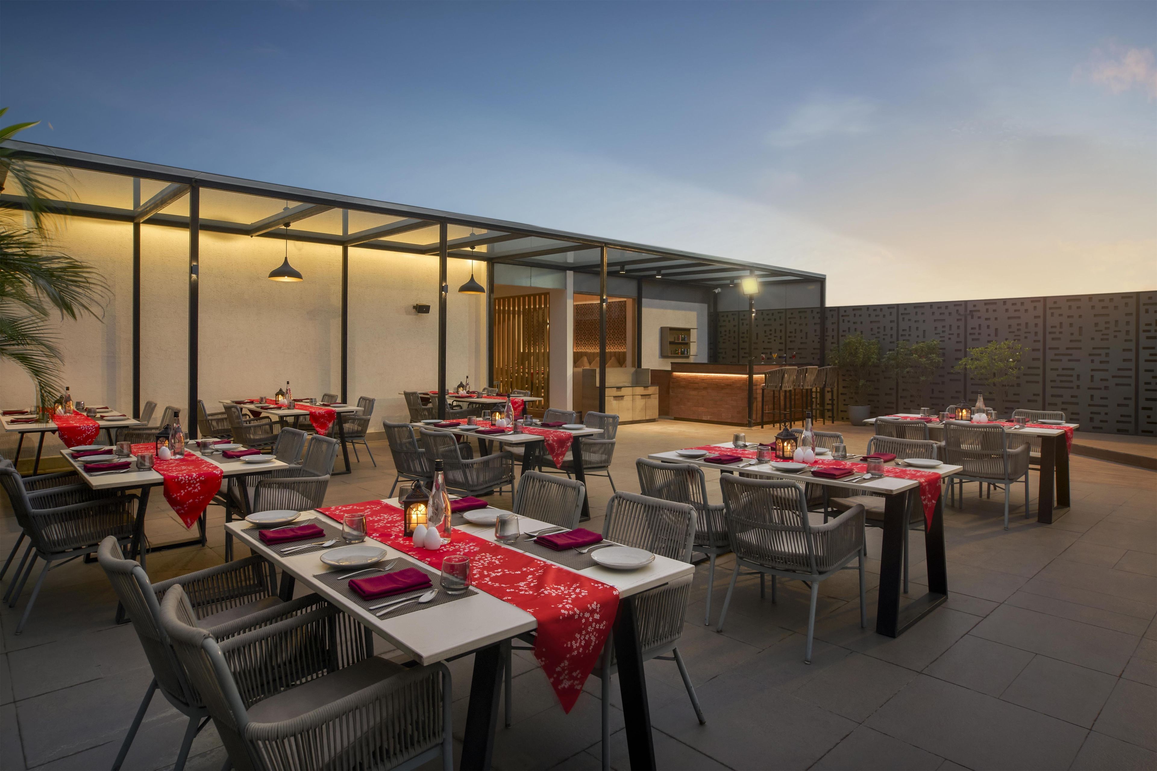 An outdoor dining area with tables set for multiple people, featuring a modern design with glass partitions and ambient lighting.