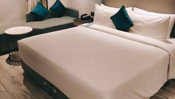 Quarto de hotel moderno com uma cama grande, um sofá pequeno, uma mesa de cabeceira e uma decoração na parede.