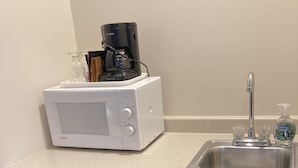 A compact kitchenette with a white microwave, a coffee maker, a sink, and a dishwasher. - Hotel Pratt- Cooperstown, NY- Baseball Central- Downtown- (Cooperstown)