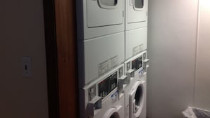 A laundry room with stacked washers and dryers, control panels, and a door. - Hotel Pratt- Cooperstown, NY- Baseball Central- Downtown- (Cooperstown)