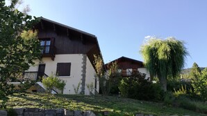 Una casa de dos pisos con base de piedra, un balcón de madera y un jardín exuberante.