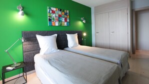 Ein Zimmer mit zwei Betten, einer grünen Wand, einem farbenfrohen abstrakten Gemälde und einer geschlossenen Tür.