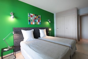 A room with two beds, a green wall, a colorful abstract painting, and a closed door.