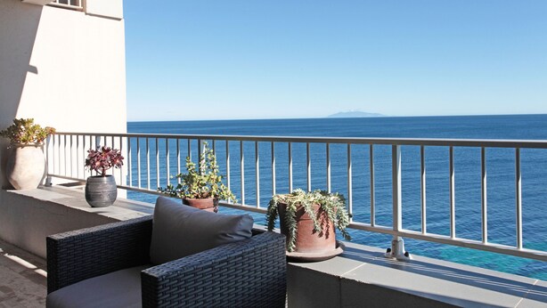 Ein Balkon mit Korbmöbeln, Topfpflanzen und Blick aufs Meer.