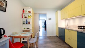 Eine kleine Küche mit Essbereich, mit einem Holztisch, roten Stühlen und einem weißen Regal mit verschiedenen Küchenutensilien.