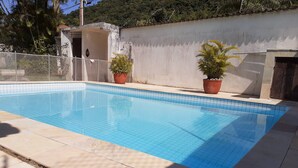 Une piscine rectangulaire aux carreaux bleus, entourée d’une terrasse également carrelée. Deux plantes en pot sont posées sur la terrasse.