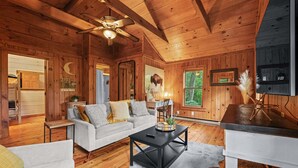A wooden cabin interior with a sofa, coffee table, and a television on a stand.