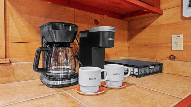 A coffee maker, two coffee cups, and a toaster on a kitchen counter.