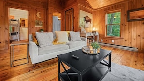 A cozy cabin interior with a sofa, a coffee table, and a large window offering a view of the outdoors.