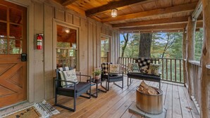A wooden porch with a fire extinguisher, a welcome mat, and outdoor seating with cushions.