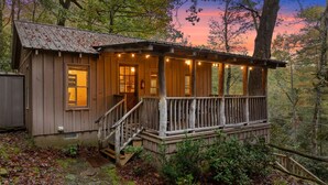 A rustic cabin with a wooden deck, a staircase, and a porch with string lights.
