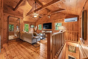 A wooden cabin interior with a sofa, dining table, and ceiling fan.