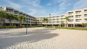 Ein Beachvolleyballfeld mit Netz, umgeben von Palmen und einem Hotel im Hintergrund.