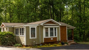 Une maison mobile de plain-pied, dotée d’un porche à l’avant et entourée d’une forêt dense.