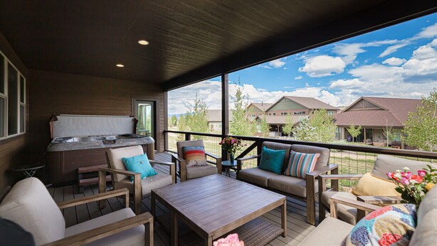 A covered outdoor patio with a hot tub, seating area, and a view of surrounding houses.