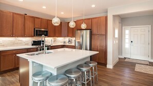 A modern kitchen with wooden cabinets, stainless steel appliances, a large island with bar stools, and pendant lighting.