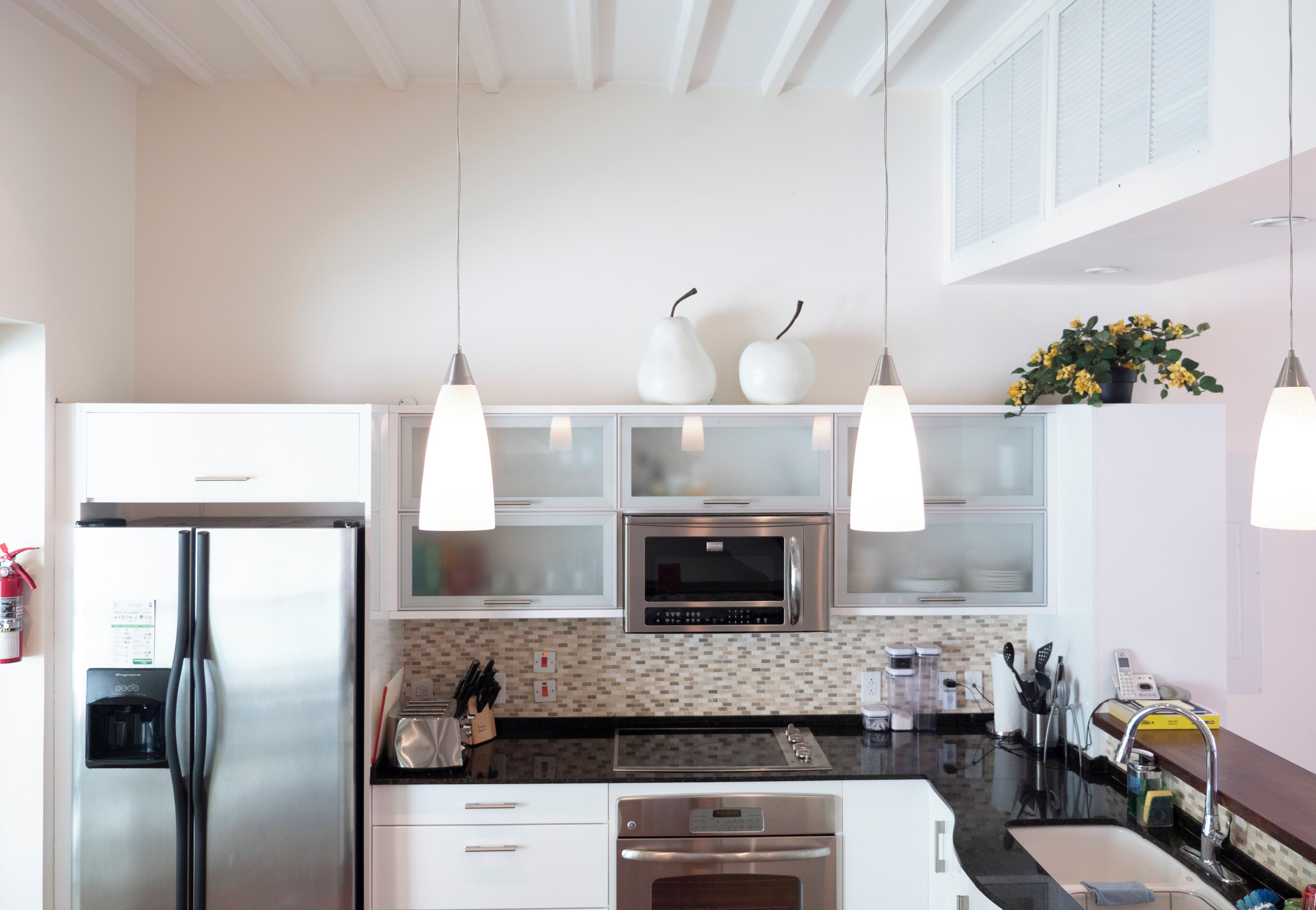 Una cocina moderna con electrodomésticos de acero inoxidable, armarios blancos e iluminación colgante.