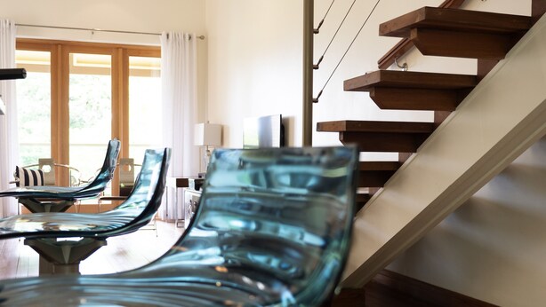 Een modern interieur met een trap, een eethoek met glazen stoelen en een uitzicht door grote ramen.