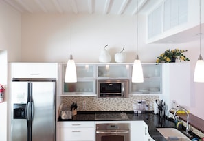 Cozinha moderna com eletrodomésticos de aço inoxidável, armários brancos e iluminação pendente.