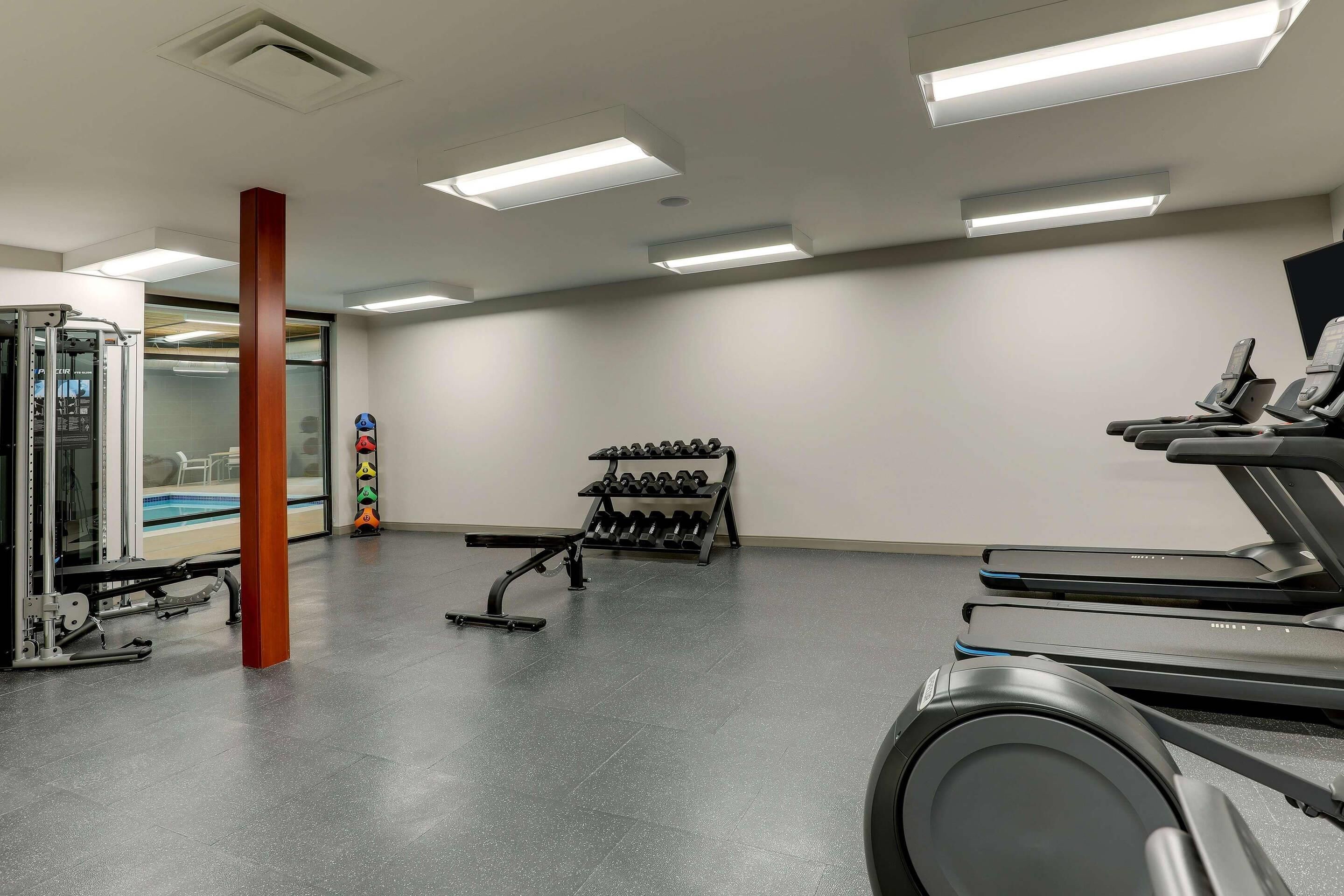 Ein Fitnessraum mit Laufbändern, Kraftgeräten und einer Hantelbank.