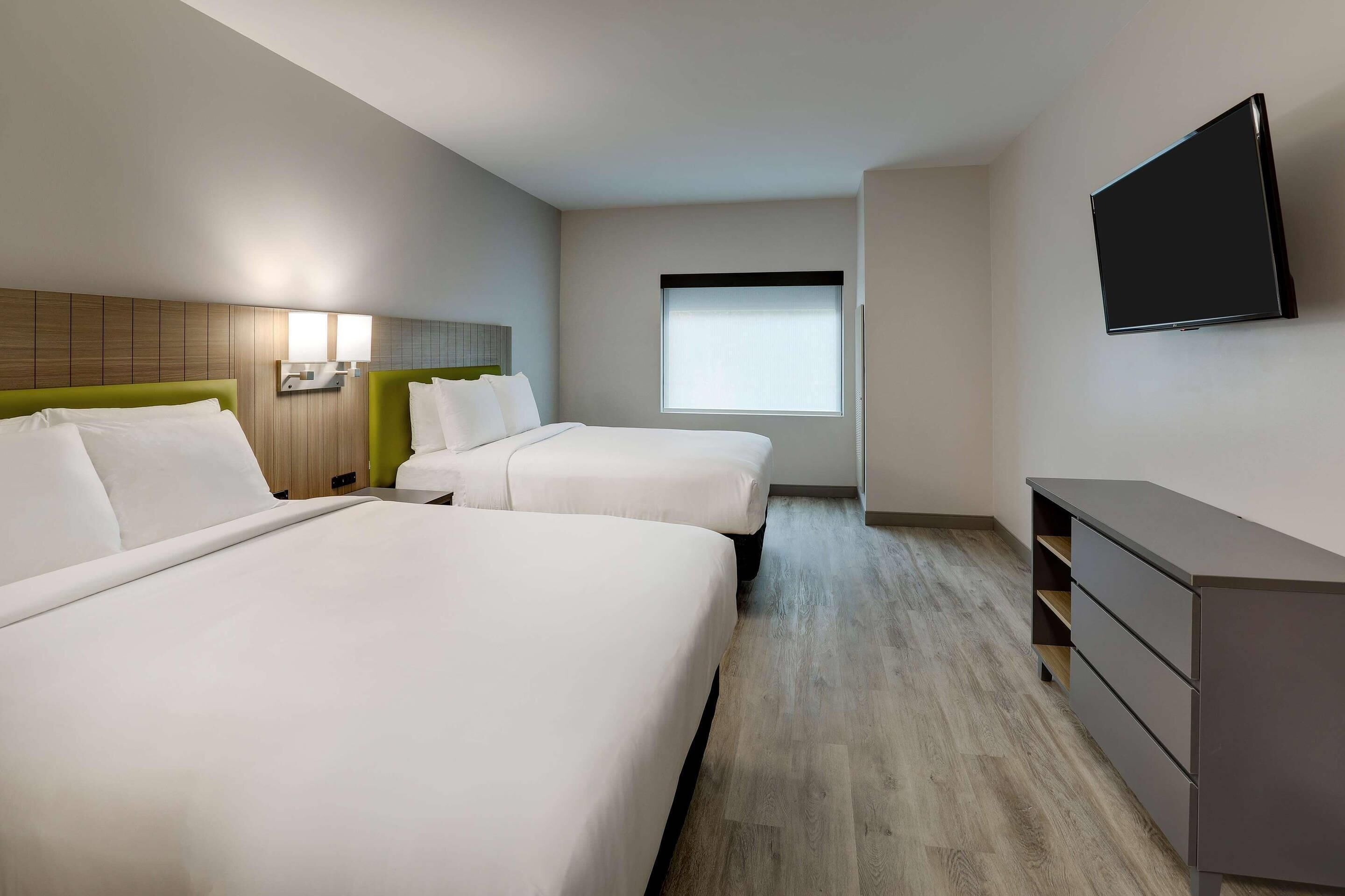Ein Hotelzimmer mit zwei Betten, einem Schreibtisch, einem Fernseher und einem Fenster.