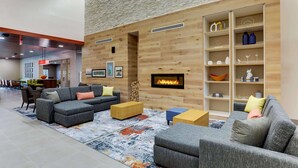 A modern living room with a fireplace, grey sofas, wooden shelves, and a patterned rug.