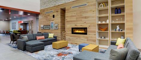 A modern living room with a fireplace, grey sofas, wooden shelves, and a patterned rug.