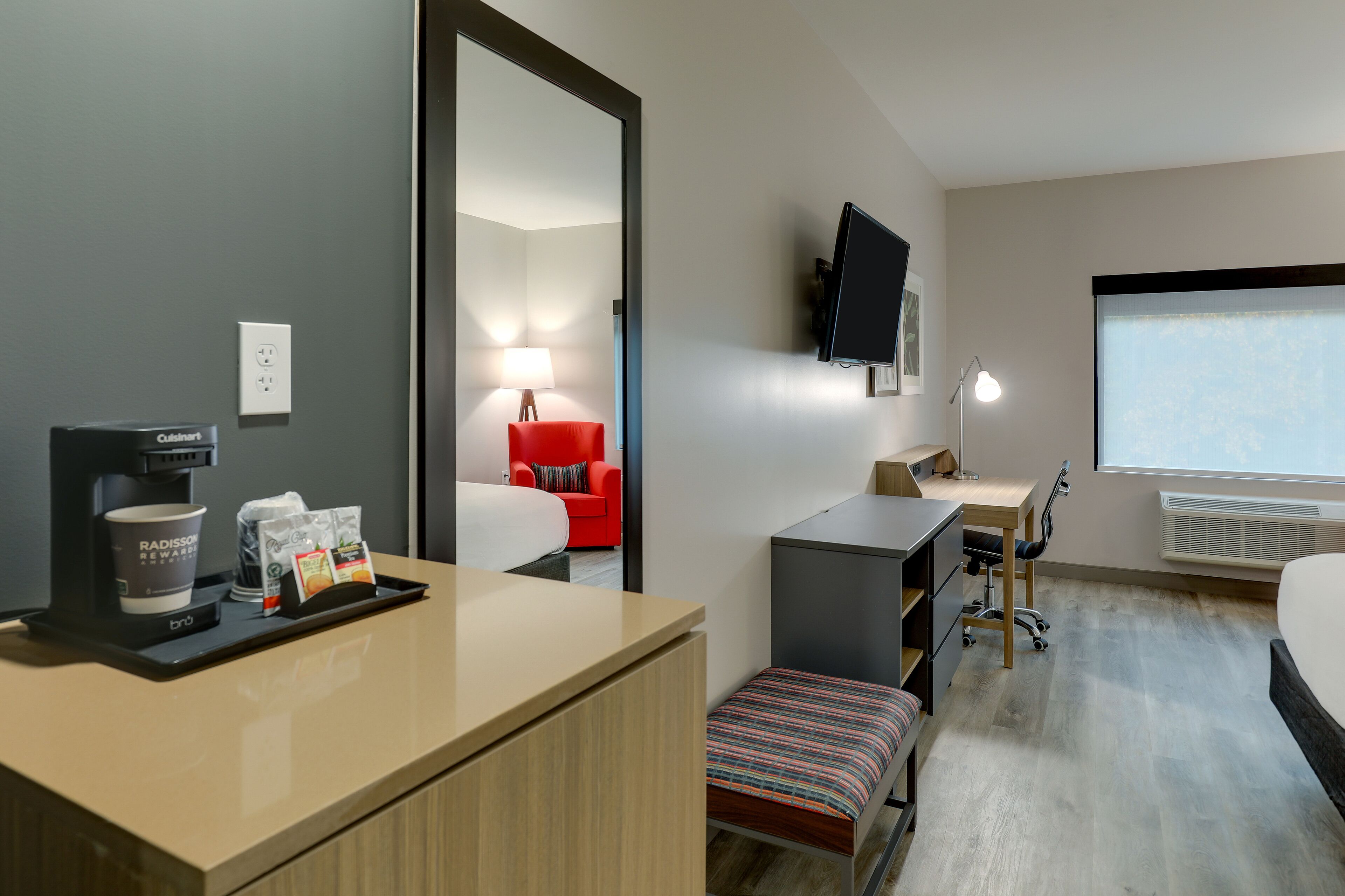 Una habitación de hotel con cama, escritorio, silla, televisión y cafetera.