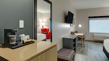 Una habitación de hotel con cama, escritorio, silla, televisión y cafetera.