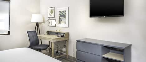 A hotel room with a bed, desk, chair, TV, and storage unit.