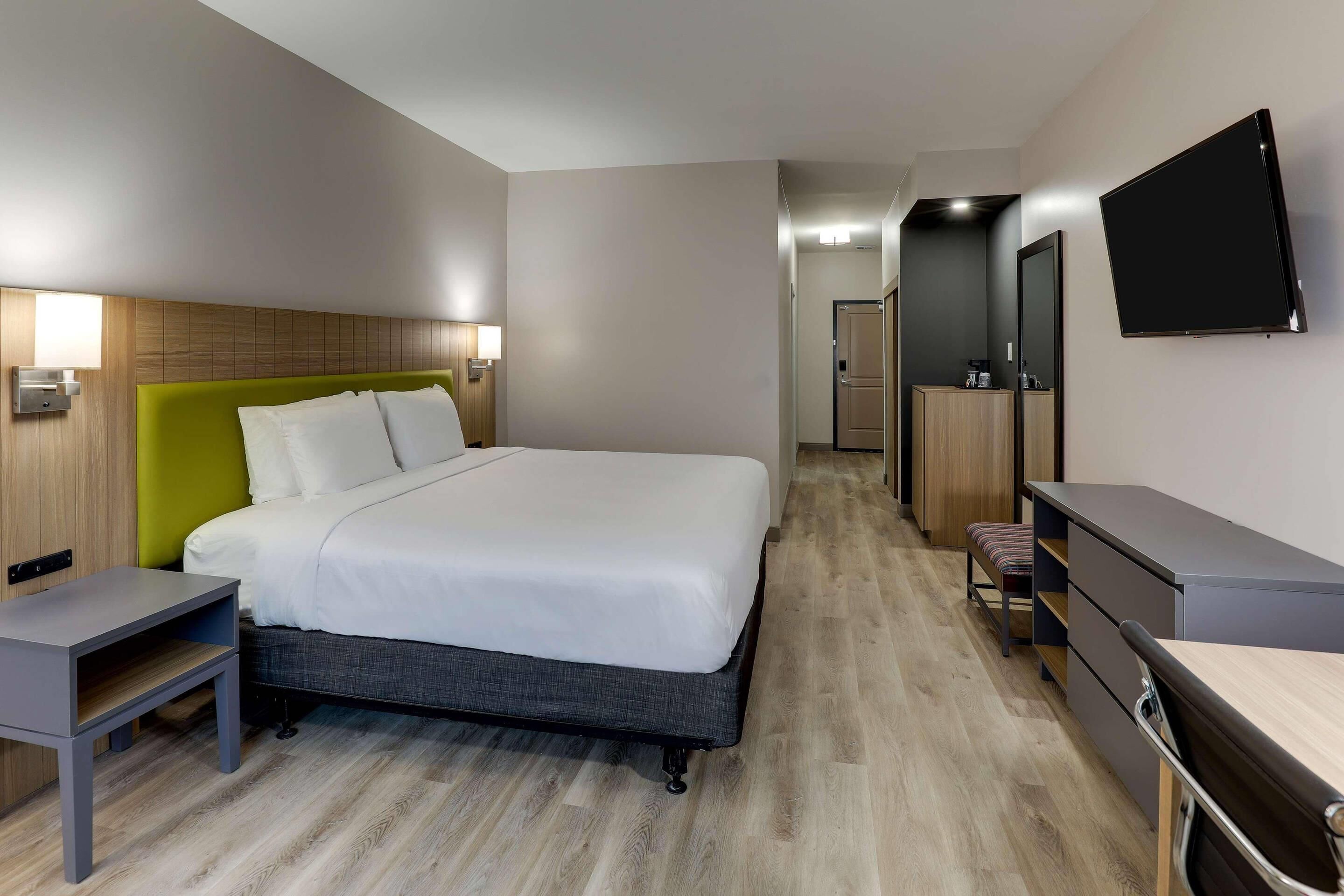 A hotel room with a bed, bedside table, desk, chair, TV, and a mirror.