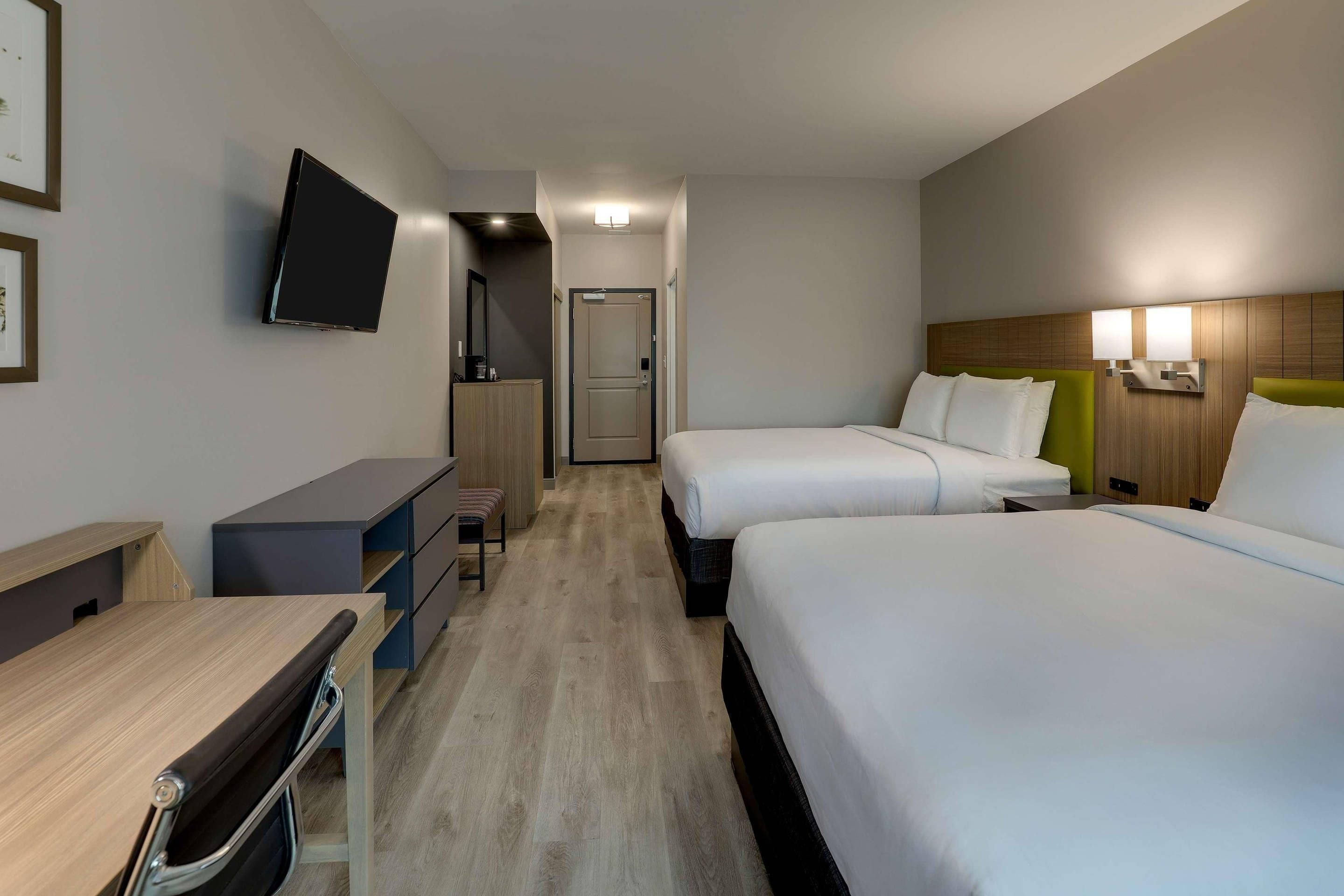 Ein Hotelzimmer mit Schreibtisch, zwei Betten, einem Fernseher und einer Tür.