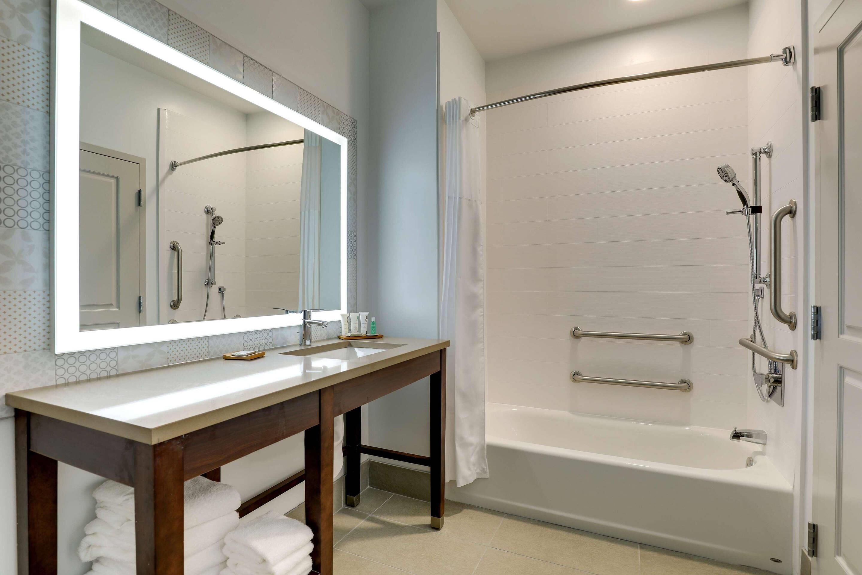 A bathroom with a shower, a sink, a mirror, and a towel rack.