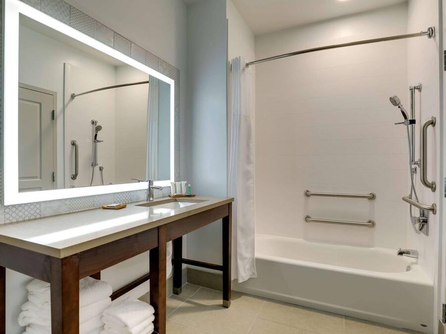A bathroom with a shower, a sink, a mirror, and a towel rack.