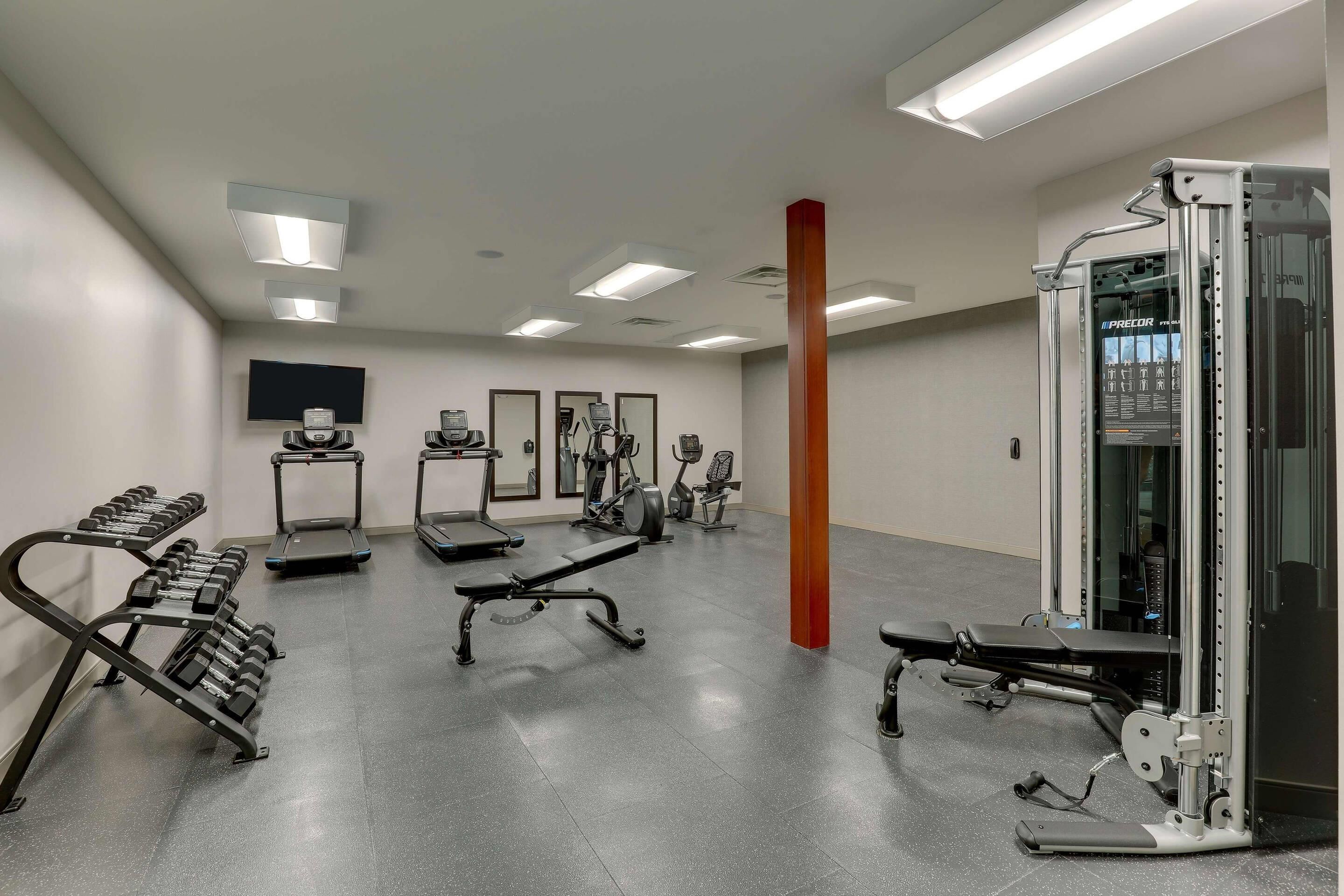 Une salle de sport équipée de tapis de course, de bancs de musculation et d’une machine à câbles.