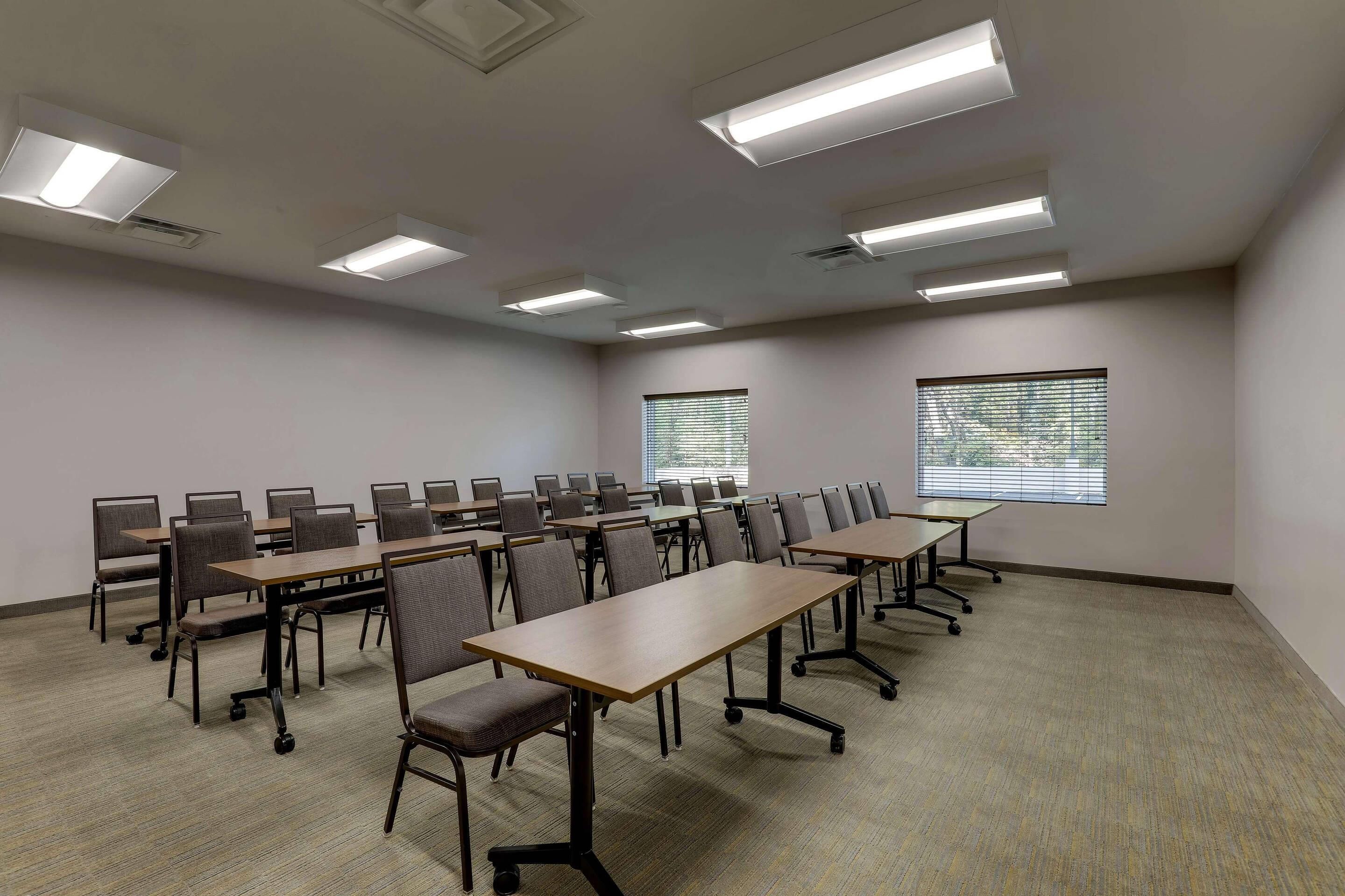 A conference room with multiple tables and chairs, ceiling lights, and windows.