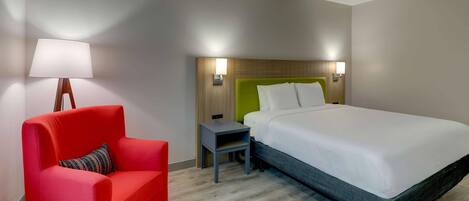 A hotel room with a bed, a red chair, a nightstand, and a lamp.
