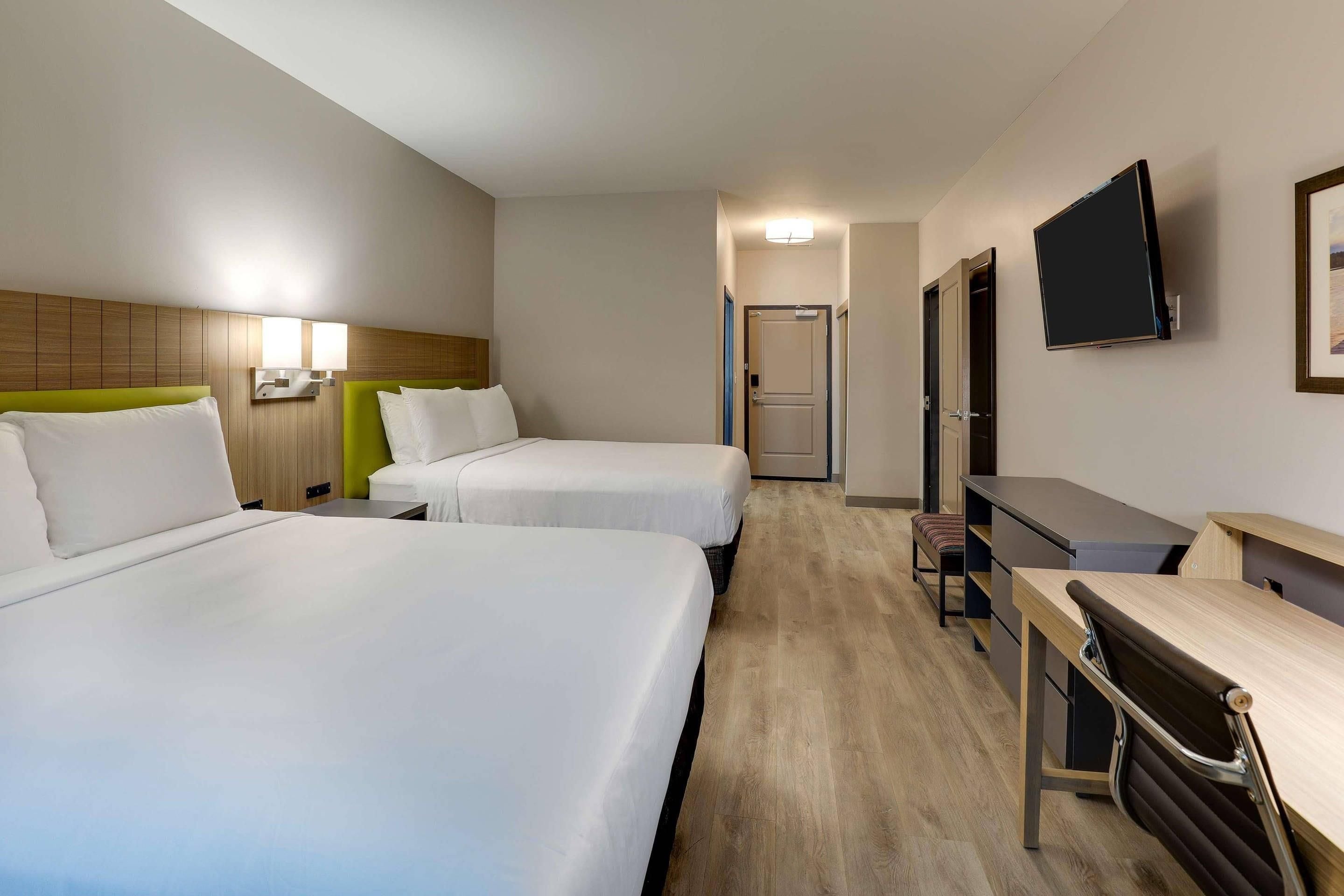 A hotel room with two beds, a desk, a chair, a TV, and a door.