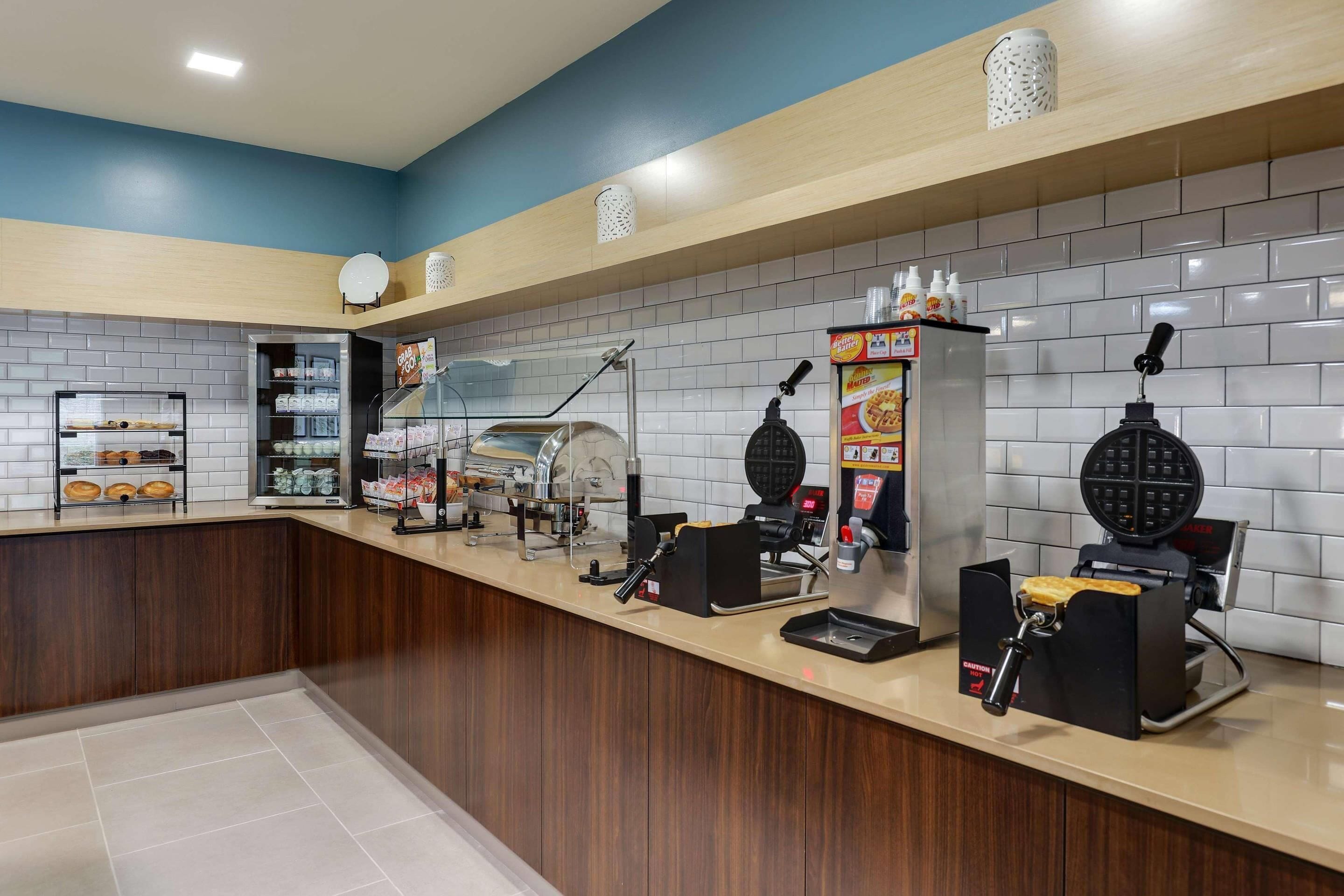 A clean, modern kitchen area with a waffle maker, coffee machine, and various food items on display.