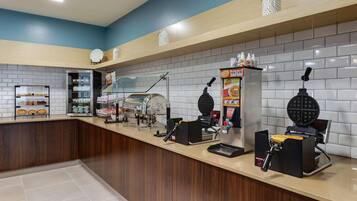 A clean, modern kitchen area with a waffle maker, coffee machine, and various food items on display.